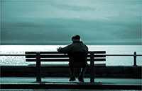 Elderly gentleman sitting on a bench facing the water.