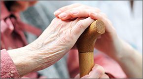 Elder and young hands on top of a cane.