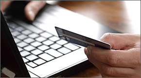 Hand holding credit card while working on a laptop.