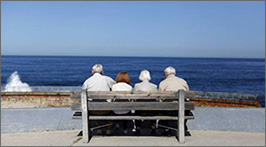 Elderly couples sitting on a bench with the ocean in front of them