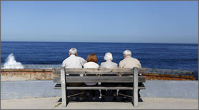 Two senior couples sitting on a bench facing the ocean