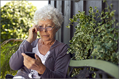 Gray haired women sitting on a bench looking at her phone